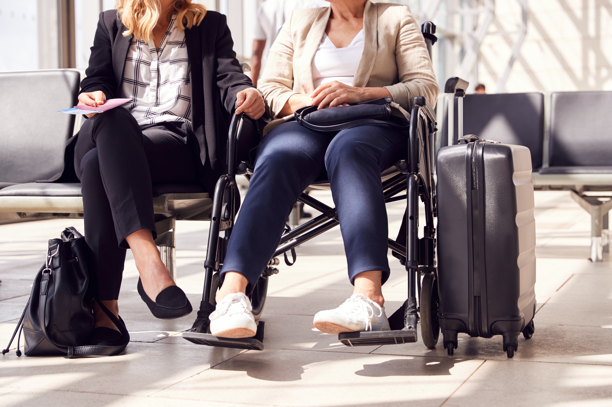 Close Up Of Businesswoman Sitting In Airport Departure With Female Colleague In Wheelchair