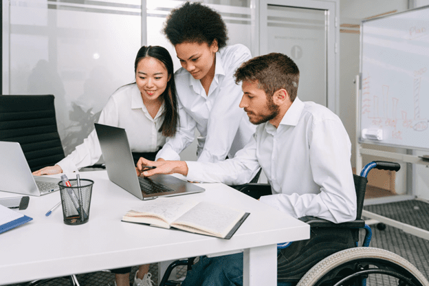 Man in wheel chair presenting his worck to two female colleagues on a laptop at a meeting room